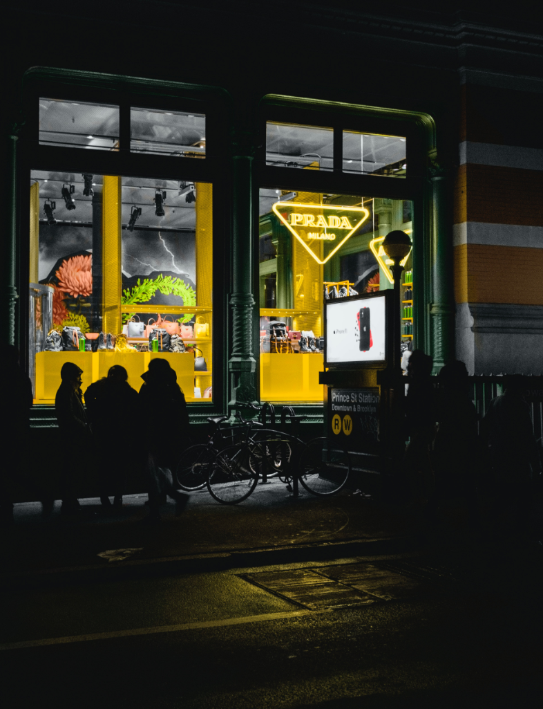 A nighttime photo of a shop with three individuals seated in front.